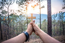 hands holding up a wooden cross outdoors 