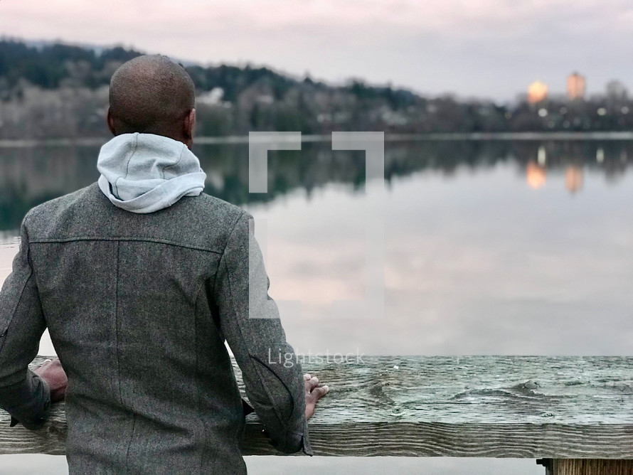 man looking out at a city scene across a lake 