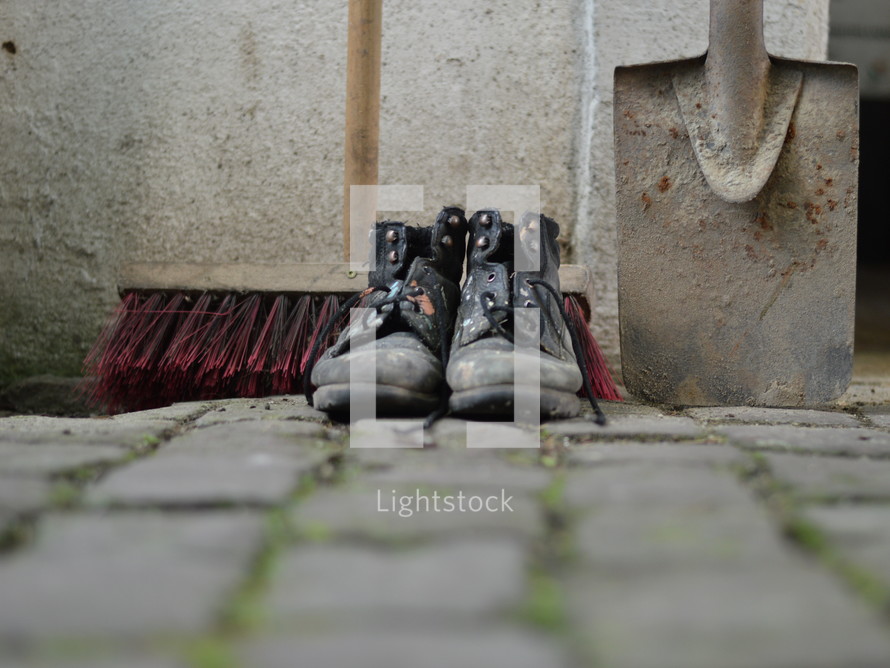 old worn painted work boots with a yard broom and a spade