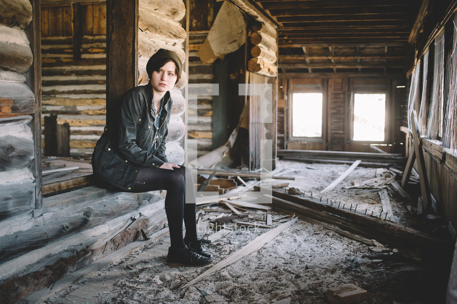 A girl sits in an abandoned log house.