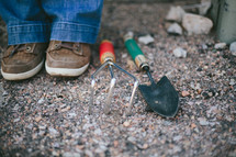 Person's feet and garden tools on a rocky ground