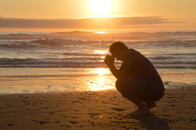 man praying at the beach in front of a sunset
