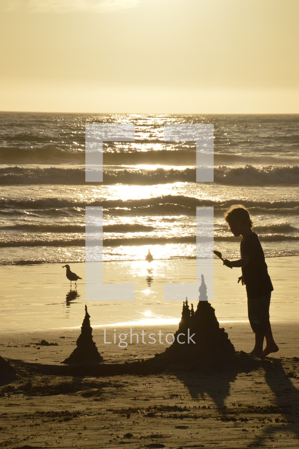 A child builds a sand castle on the beach in the light of the sunset.