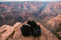 a man and woman sitting at the edge of a cliff looking out at canyons snuggling 