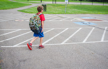 a boy wearing a red shirt walking from school across a parking lot.