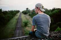 a man sitting looking down at railroad tracks 