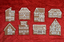 eight different self baked gingerbread house fronts with numbers on them on red velvet as part of an advent calendar