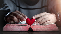 a man holding a red felt heart over a Bible 