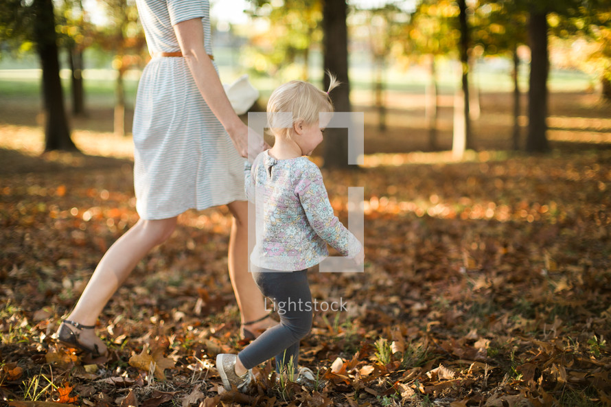 mother and daughter walking through fall leaves 