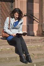 a woman sitting and reading a Bible on church steps 