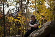 a man sitting on a rock in an autumn forest 