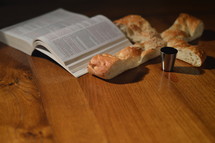 Bread in the shape of a cross with an open bible and a goblet of wine with spilled wine