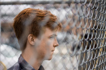 a young man standing in front of a chain link fence 