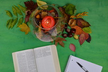notebook, open Bible, pen, candle, and fall leaves 