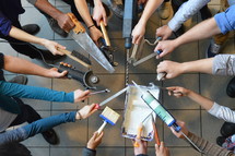 volunteers standing in a circle their hands holding tools as a symbol for: working together to fix things in the church building.