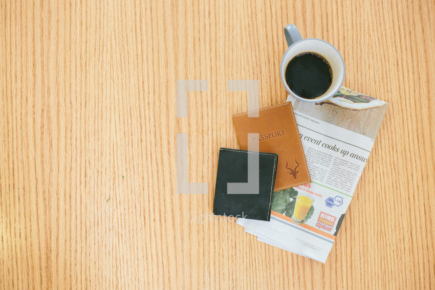 wallet, passport, newspaper, and coffee mug on a table 
