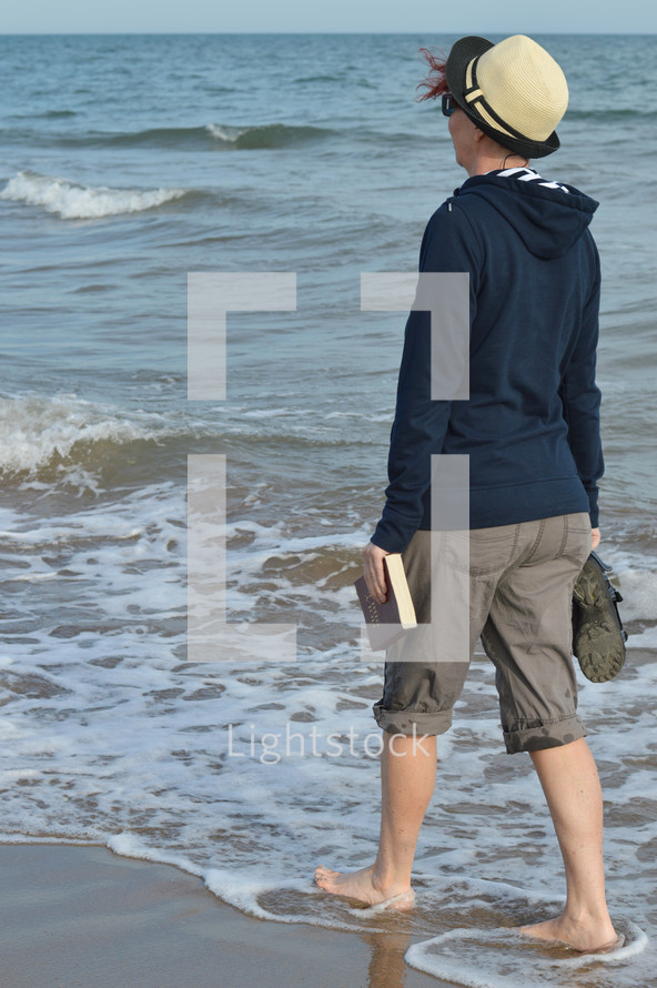 woman walking on a beach carrying a Bible 