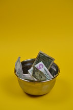 dollar bills in a bowl on a yellow background 