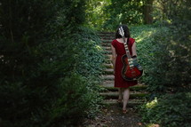 a woman in a red dress with an electric guitar walking through the dark woods 