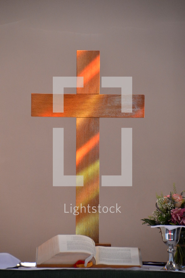 sunlight falling through a stained-glass window and illuminating a wooden cross at the altar.

