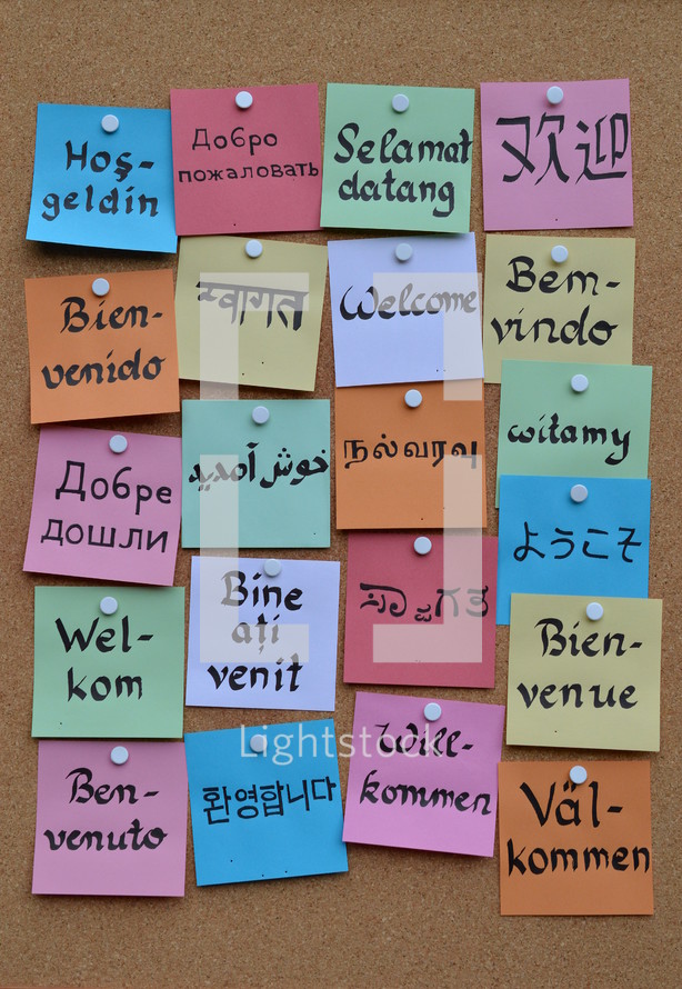 welcome in various languages on sticky notes on a cork board 