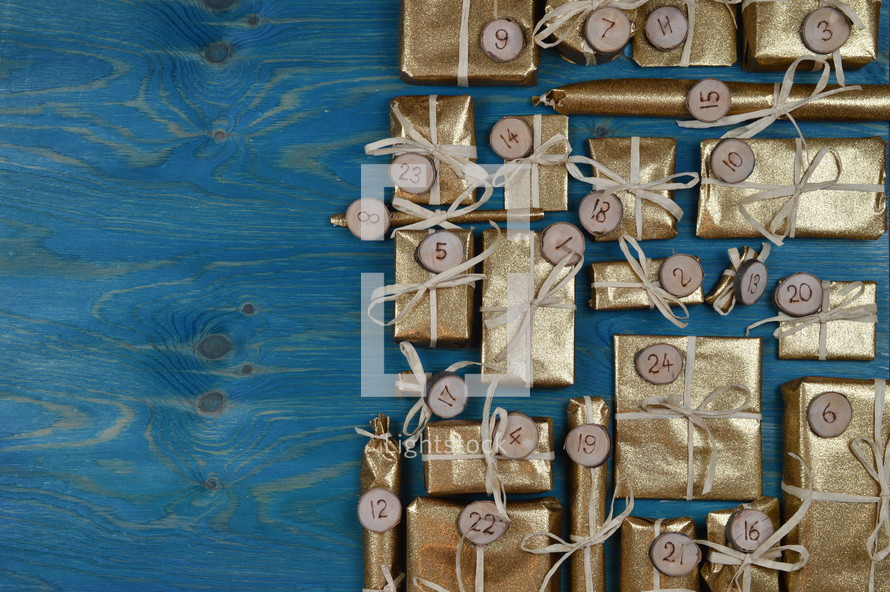 Border of advent calendar with twenty four golden presents on teal wood with negative space to the left