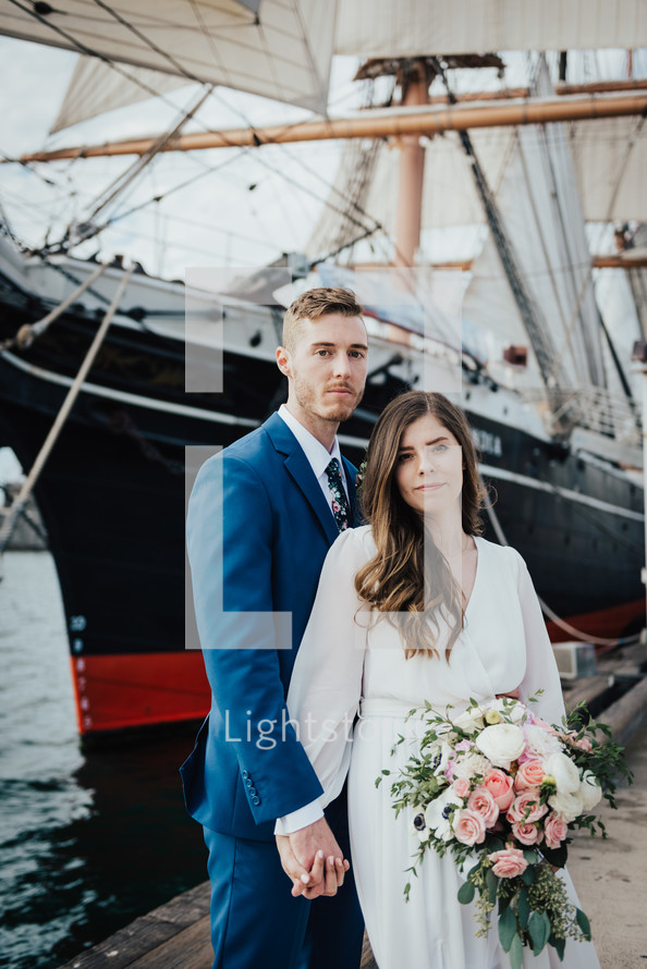 bride and groom standing in front of a ship 