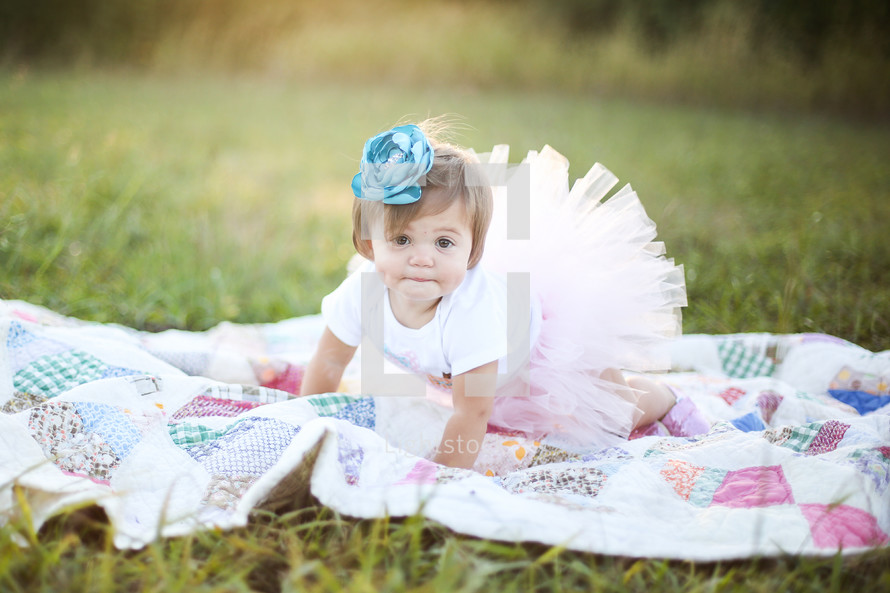a little girl in a tutu crawling on a blanket in the grass 