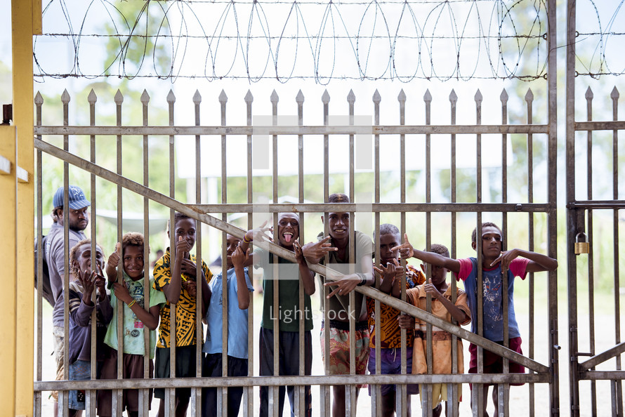 kids waving through a metal fence 