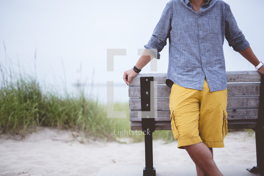 a man standing in front of a bench on a beach 