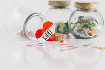Jars of paper hearts on a white background with one lettered KIND in front.