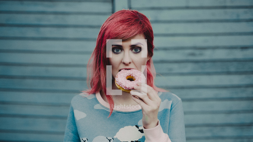 a young woman with pink hair eating a donut 
