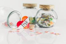 Jars of paper hearts on a white background with one lettered LOVE in front.