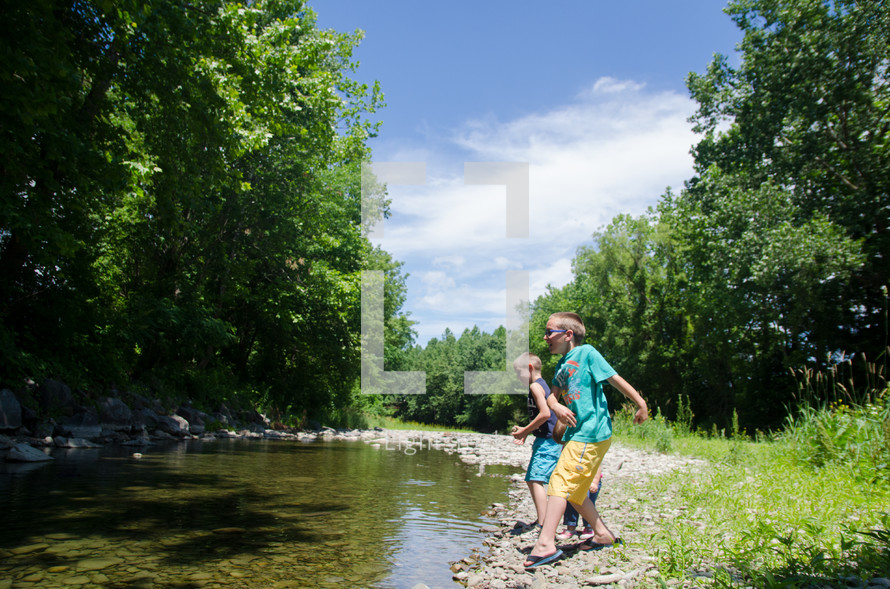 boys skipping rocks  along a creek on a warm summer day