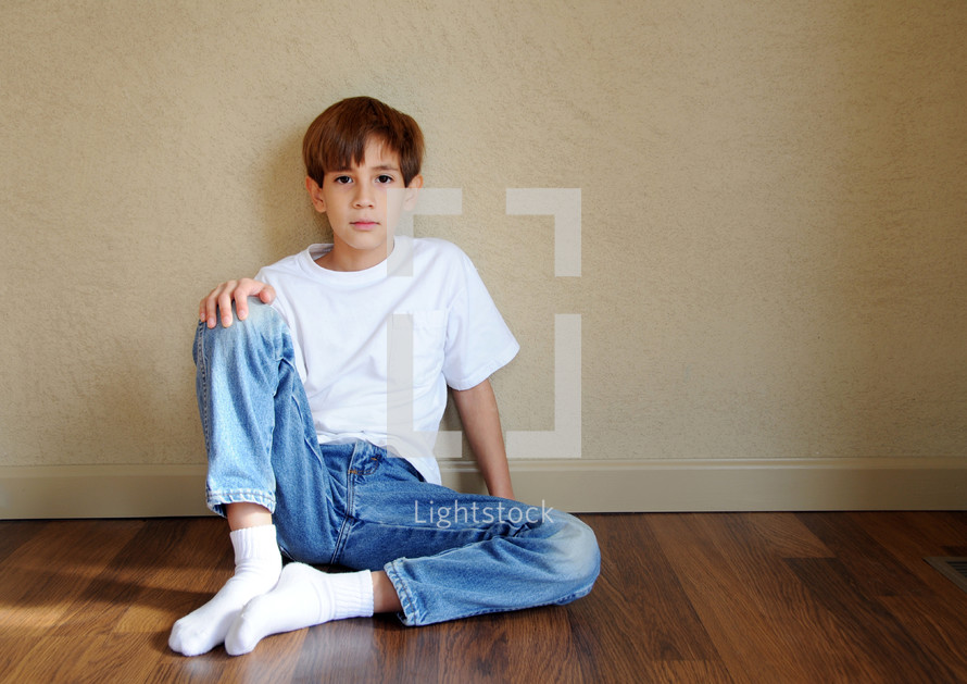 A boy sitting against a wall on a hardwood floor.