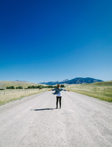 woman standing in the middle of a rural road 