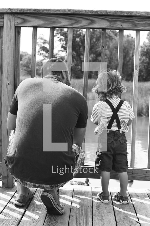 Father and son on a wooden deck overlooking a pond.