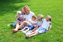 Woman, sitting on a blanket with five children, outdoors
