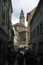 people walking on a cobblestone street with a view of a tower 