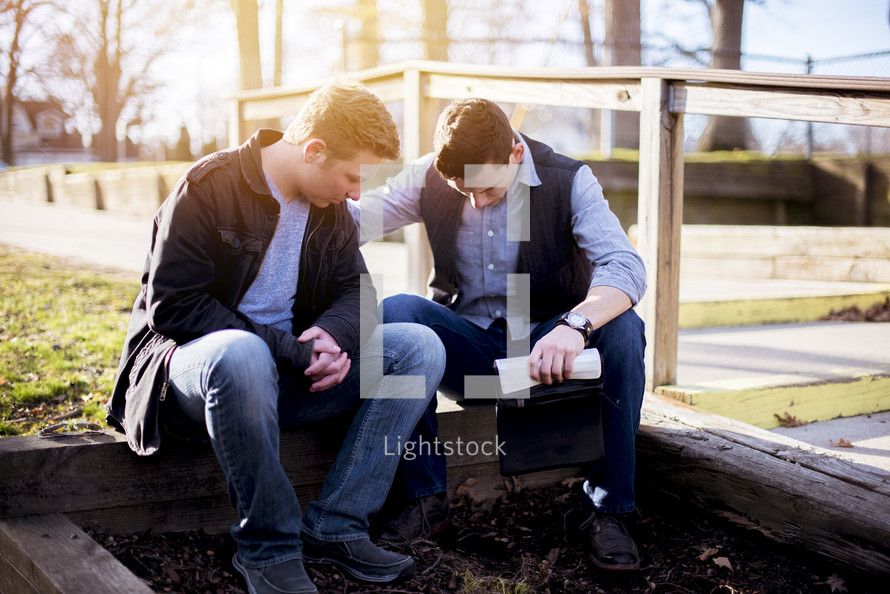 two men reading Bibles outdoors and praying 