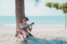 woman playing a ukulele on a beach 