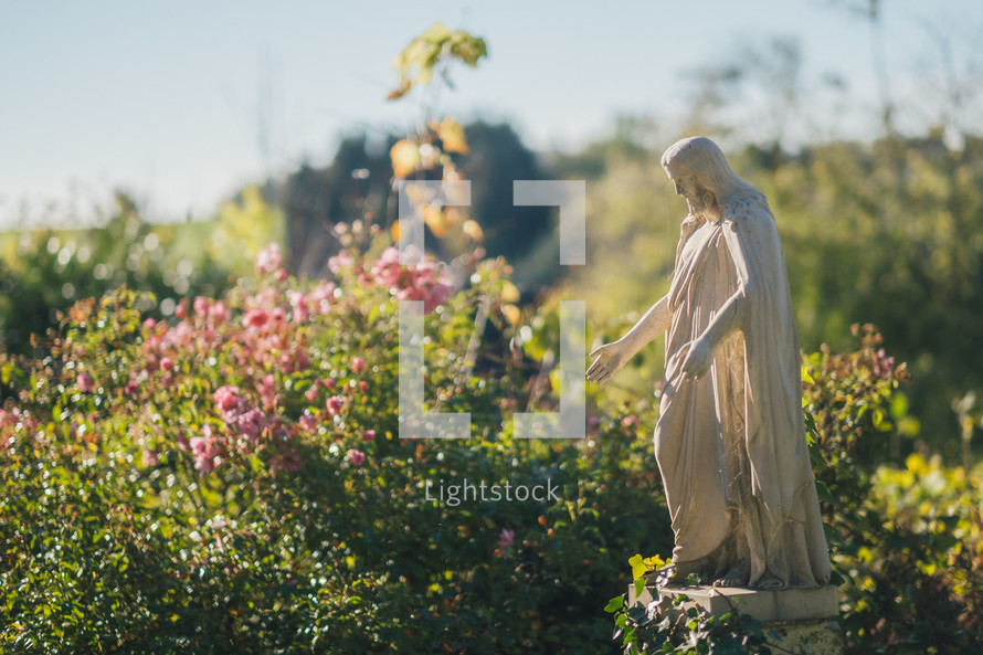 Stone Jesus stature in garden with pink flowers