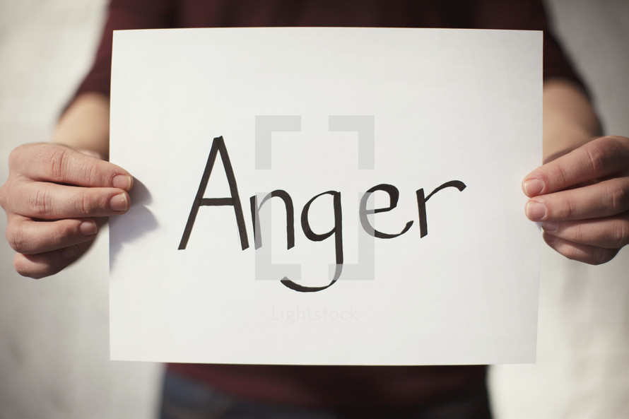 A man holding a piece of paper with the word Anger on it 