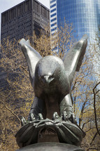 Eagle scultpute with city skyline behind trees in the background.