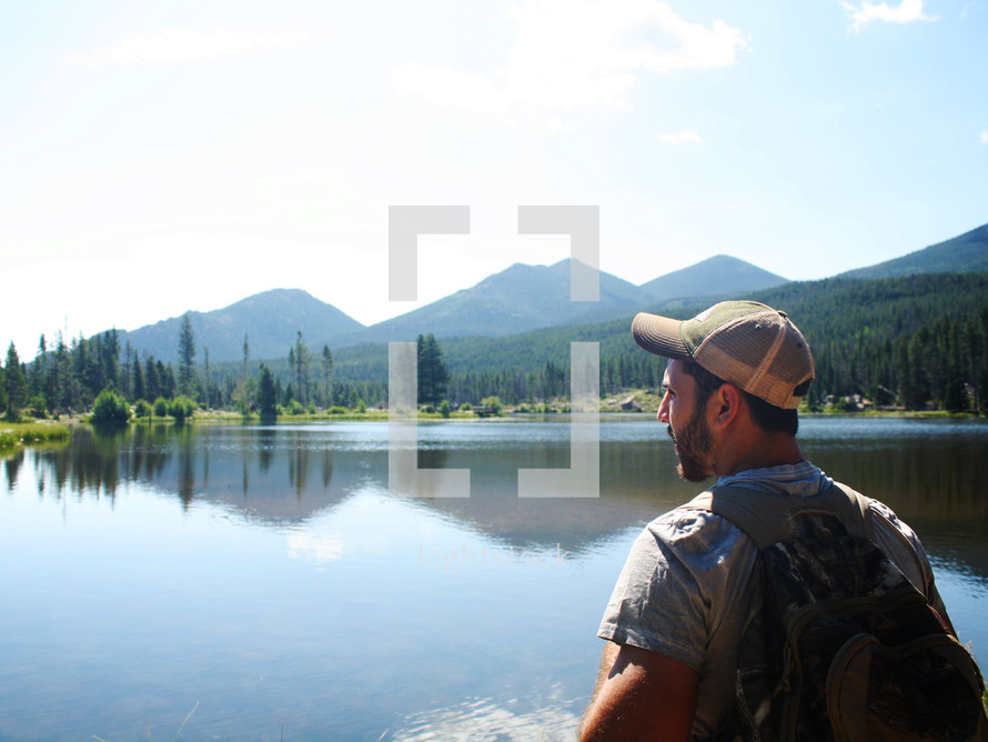a man with a backpack looking out at a lake 