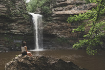 a woman sitting watching a waterfall 