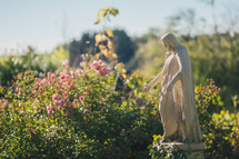 Stone Jesus stature in garden with pink flowers