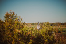 Church steeple seen through forest trees