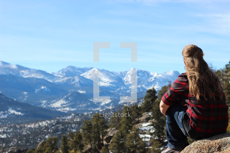 a woman sitting on a mountaintop looking out at the snowy landscape 