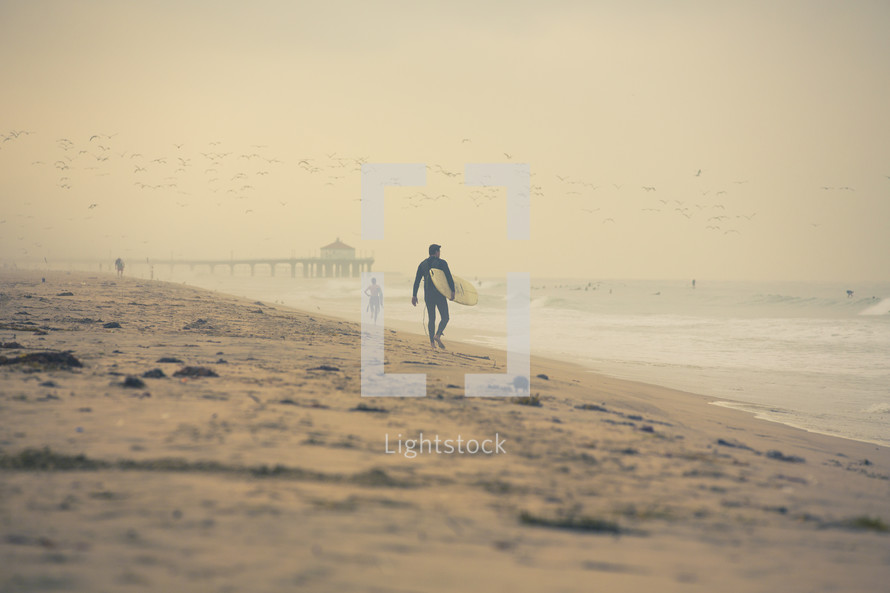 surfer walking down the beach holding a surf board